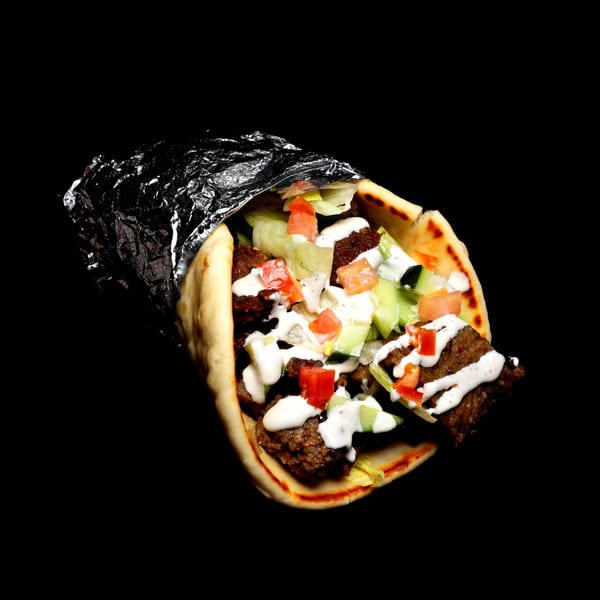 Gyro wrap with meat, lettuce, tomatoes, cucumbers, and white sauce, partially wrapped in foil.