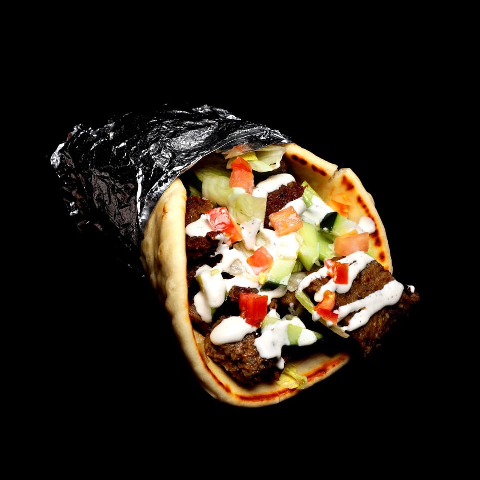Gyro wrap with meat, lettuce, tomatoes, cucumbers, and white sauce, partially wrapped in foil.