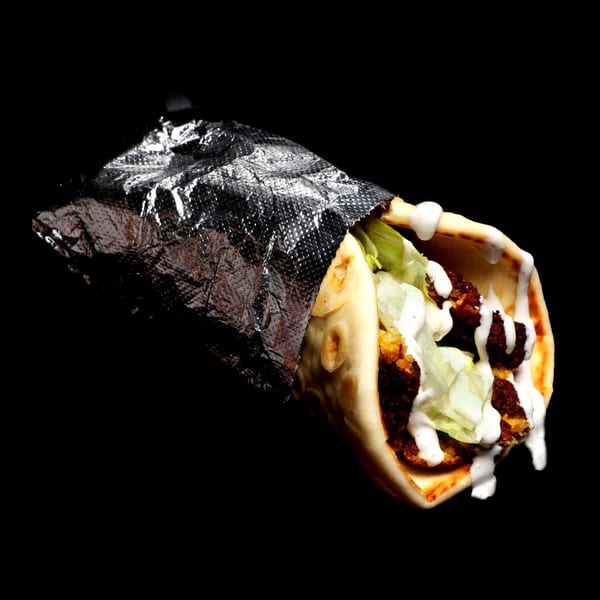 Falafel wrap with lettuce and white sauce, partially wrapped in foil, against a black background.