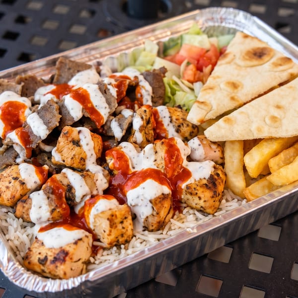 A takeout container filled with chicken and lamb over rice, salad, fries, and pita bread.