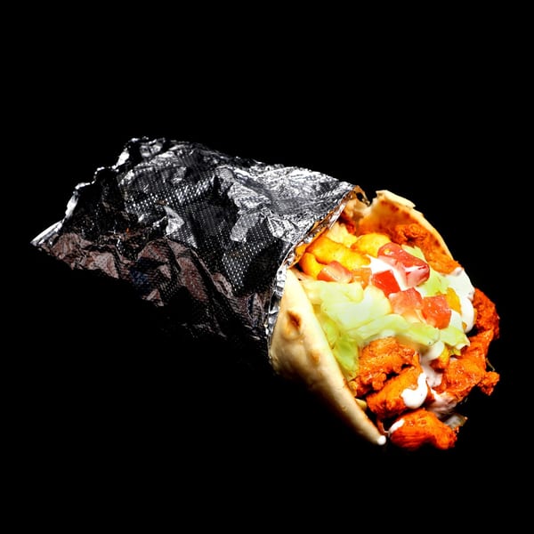Chicken shawarma wrap with fries, lettuce, tomatoes, and white sauce, partially unwrapped from foil.